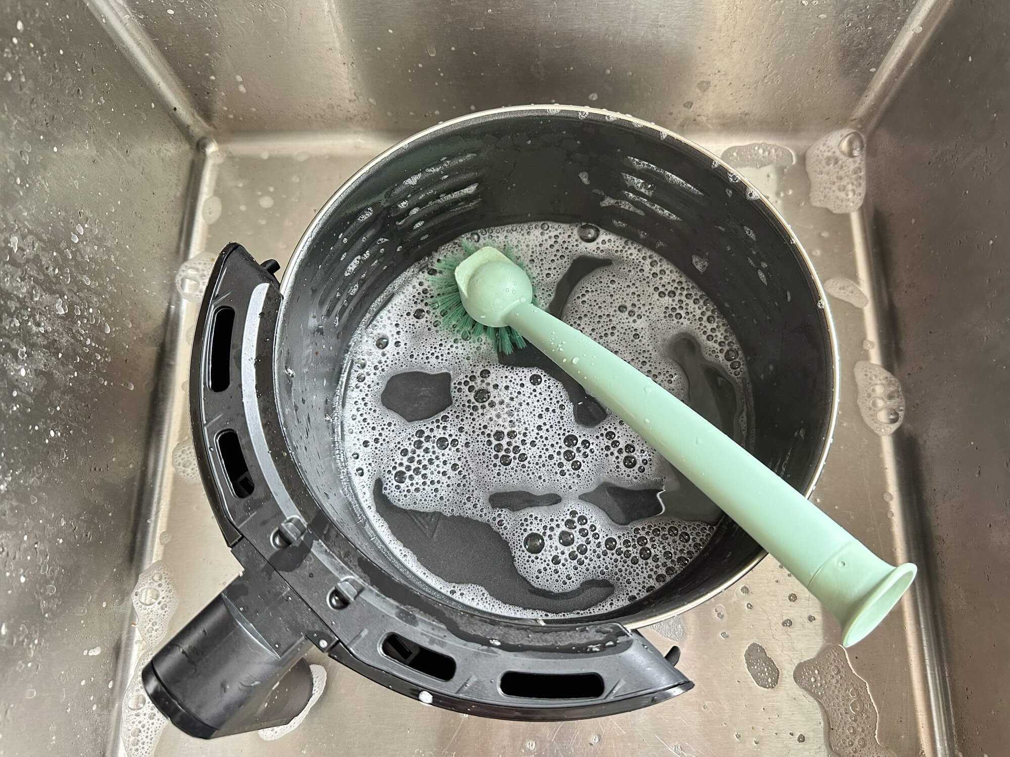 Een gootsteen gevuld met zeepsop en een groene tandenborstel die wordt schoongemaakt.